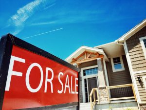 House with "For Sale" sign, blue sky.