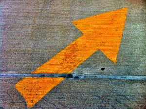 Yellow arrow painted on concrete pavement.