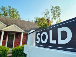 A sold sign in front of a suburban house with a person on the roof.